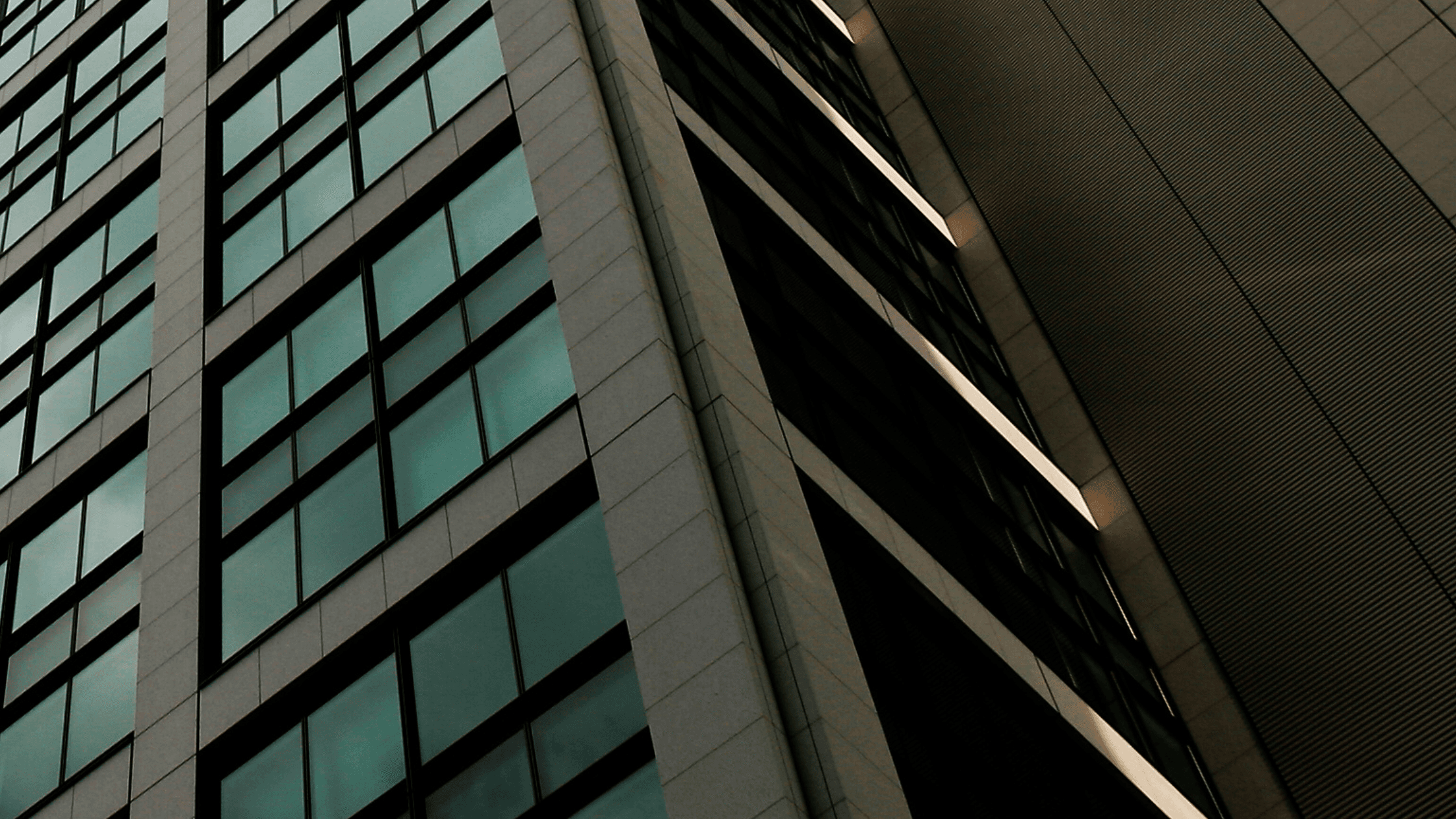 Close-up of a modern skyscraper with reflective glass windows and a textured facade, creating a geometric pattern against a dark sky.